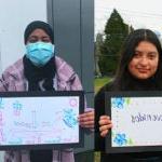 Several students pose for photos with a hand drawn sign that says welcome